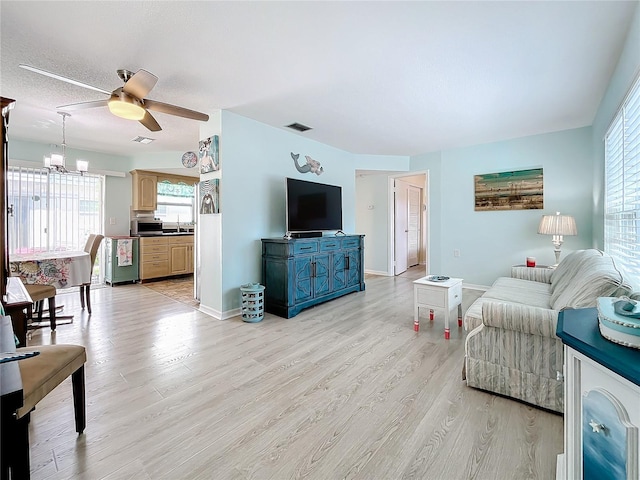 living room featuring ceiling fan with notable chandelier, sink, light wood-type flooring, and a textured ceiling