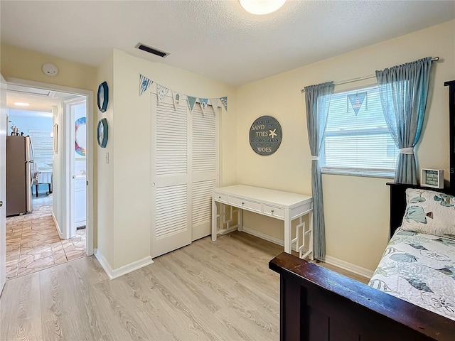 bedroom with a closet, a textured ceiling, stainless steel refrigerator, and light hardwood / wood-style flooring