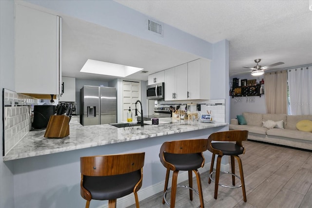 kitchen with white cabinets, a breakfast bar, kitchen peninsula, and appliances with stainless steel finishes