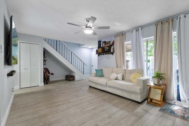 living room with a textured ceiling, ceiling fan, and light hardwood / wood-style floors