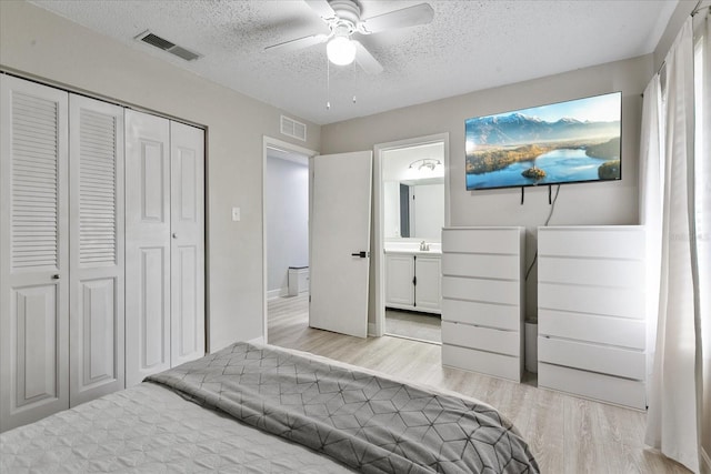 bedroom with a closet, ensuite bath, light wood-type flooring, ceiling fan, and a textured ceiling