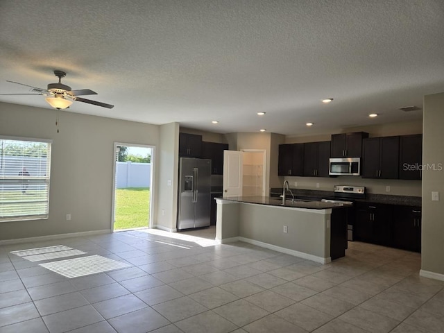 kitchen featuring a textured ceiling, light tile patterned flooring, an island with sink, appliances with stainless steel finishes, and ceiling fan