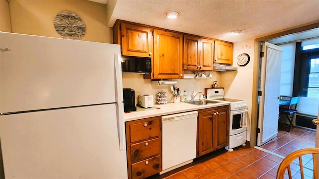 kitchen with dark tile patterned flooring, a textured ceiling, sink, range hood, and white appliances