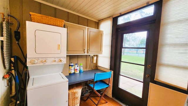 laundry area featuring light tile patterned flooring, wooden walls, cabinets, wooden ceiling, and stacked washer and dryer