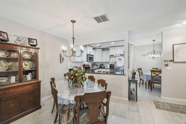 dining space with light hardwood / wood-style floors, a textured ceiling, and an inviting chandelier