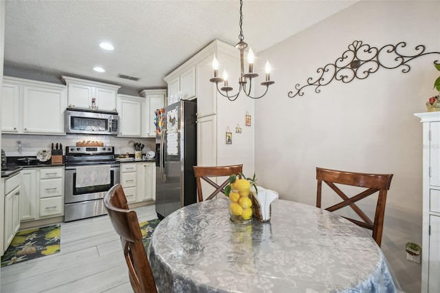 kitchen featuring tasteful backsplash, stainless steel appliances, pendant lighting, a notable chandelier, and light hardwood / wood-style flooring