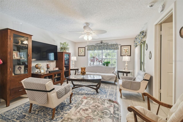 living room with light hardwood / wood-style floors, a textured ceiling, and ceiling fan