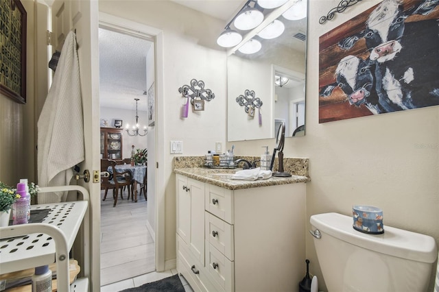 bathroom featuring hardwood / wood-style floors, an inviting chandelier, a textured ceiling, toilet, and vanity