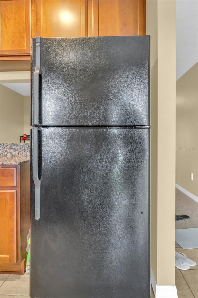 interior space featuring light tile patterned floors, stone countertops, and black fridge