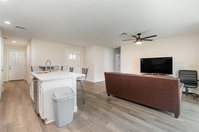 kitchen with light hardwood / wood-style floors, a kitchen island with sink, sink, and white cabinets