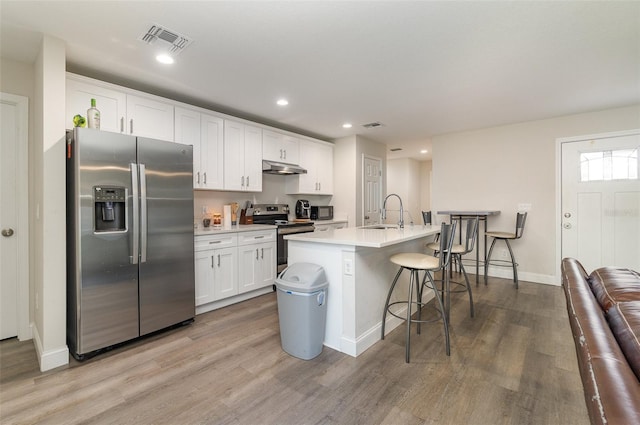 kitchen with light hardwood / wood-style floors, an island with sink, white cabinets, a breakfast bar area, and stainless steel appliances