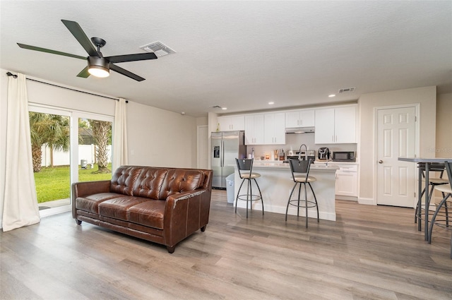 living room with ceiling fan, a textured ceiling, light hardwood / wood-style flooring, and sink