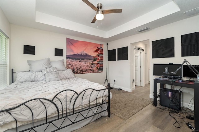 bedroom featuring ceiling fan, light wood-type flooring, and a tray ceiling