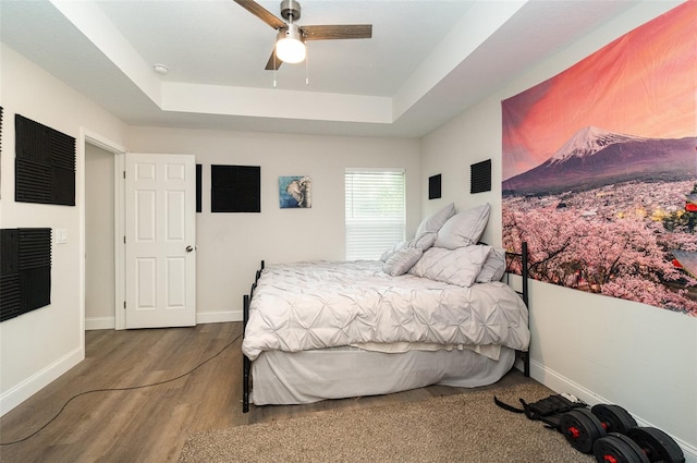 bedroom with a raised ceiling, hardwood / wood-style floors, and ceiling fan