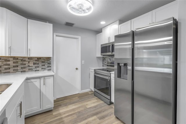 kitchen featuring white cabinetry, backsplash, stainless steel appliances, and light wood-type flooring