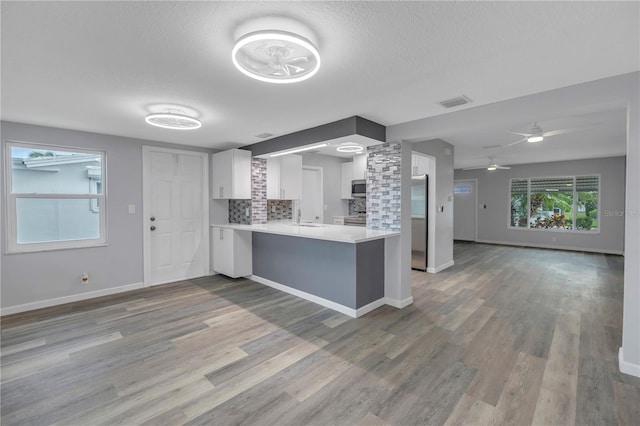 kitchen with appliances with stainless steel finishes, white cabinetry, backsplash, light hardwood / wood-style floors, and kitchen peninsula