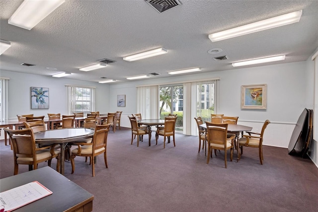 dining space with a textured ceiling, dark colored carpet, and plenty of natural light