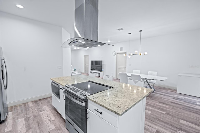 kitchen featuring white cabinets, a kitchen island, wall chimney range hood, appliances with stainless steel finishes, and decorative light fixtures