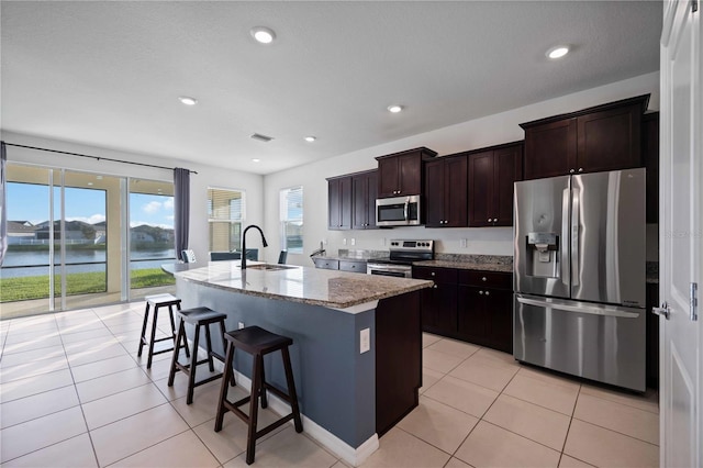 kitchen with a breakfast bar, sink, a water view, a center island with sink, and appliances with stainless steel finishes