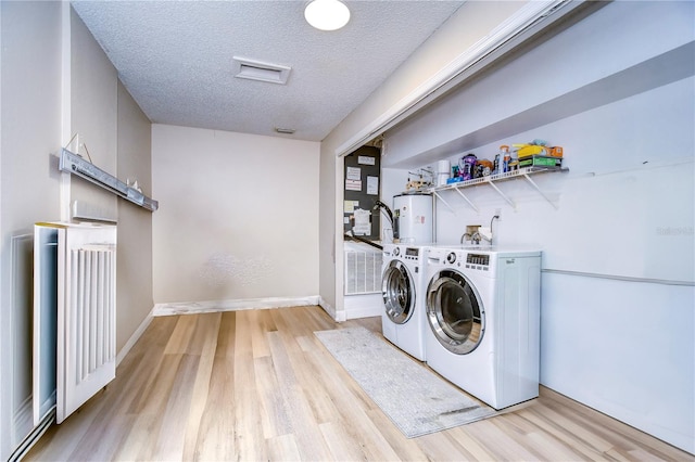 laundry area with a textured ceiling, washing machine and dryer, light hardwood / wood-style flooring, and electric water heater