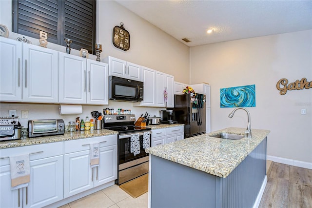 kitchen featuring sink, a center island with sink, white cabinetry, black appliances, and light hardwood / wood-style floors