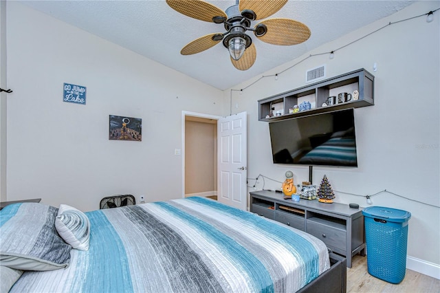 bedroom featuring ceiling fan, a textured ceiling, light wood-type flooring, and vaulted ceiling