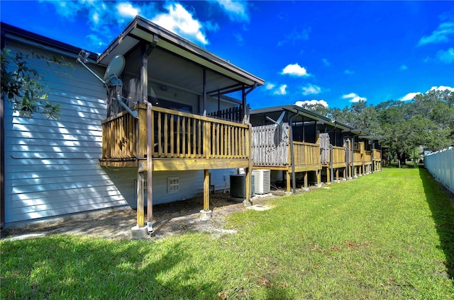 back of property with a sunroom, central AC unit, a deck, and a yard