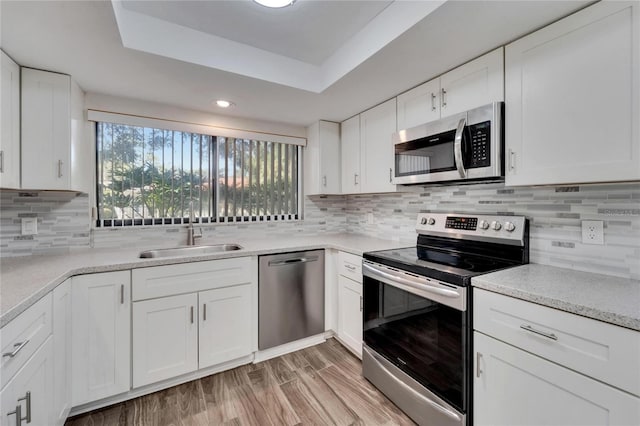 kitchen featuring appliances with stainless steel finishes, white cabinetry, a raised ceiling, light wood-type flooring, and sink