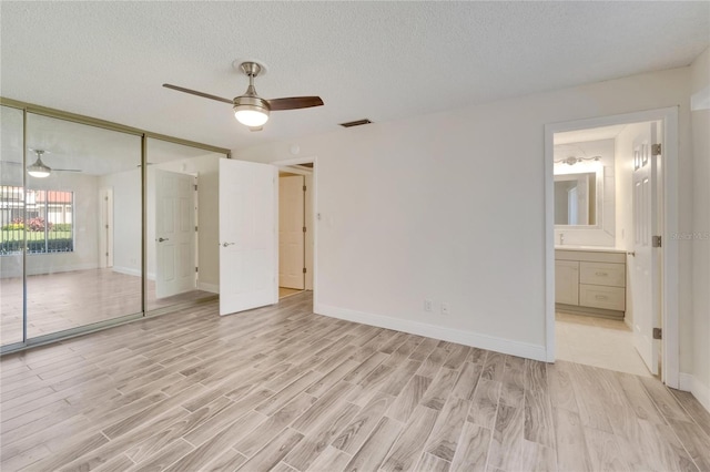 unfurnished bedroom with light wood-type flooring, a closet, a textured ceiling, ensuite bathroom, and ceiling fan