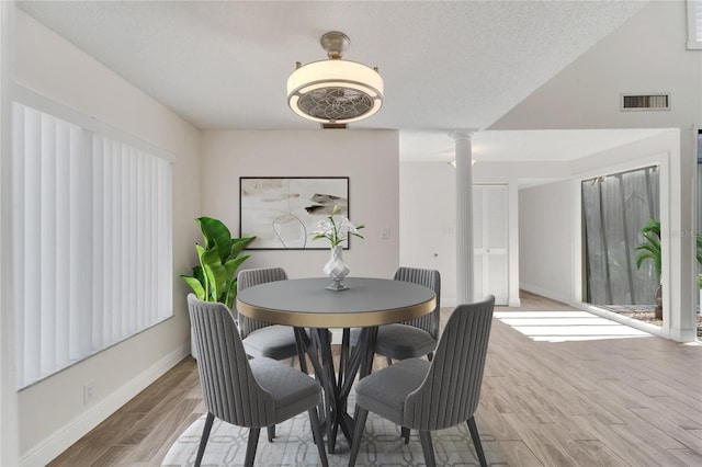 dining room with wood-type flooring, a textured ceiling, and decorative columns