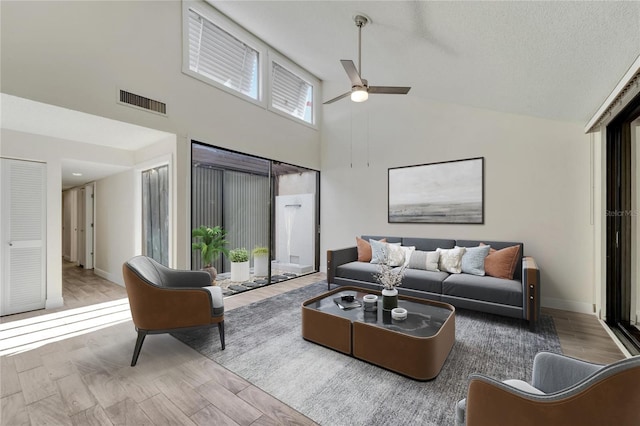 living room with ceiling fan, a textured ceiling, light hardwood / wood-style flooring, and high vaulted ceiling