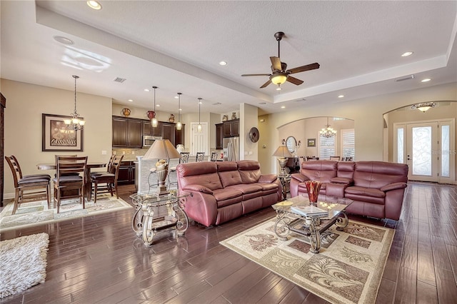 living room featuring ceiling fan with notable chandelier, a textured ceiling, a raised ceiling, and dark hardwood / wood-style flooring