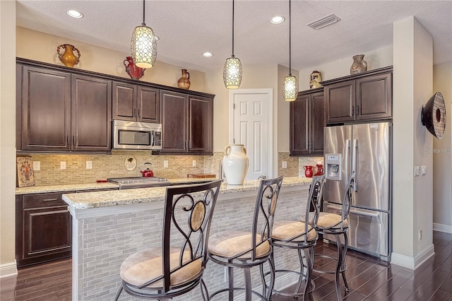 kitchen featuring hanging light fixtures, a textured ceiling, stainless steel appliances, a center island, and dark hardwood / wood-style flooring