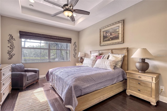 bedroom with a tray ceiling, ceiling fan, and dark wood-type flooring