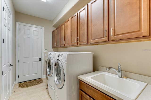 laundry room with washer and clothes dryer, cabinets, light hardwood / wood-style flooring, and sink