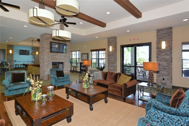 living room featuring ceiling fan, a stone fireplace, beamed ceiling, and hardwood / wood-style floors