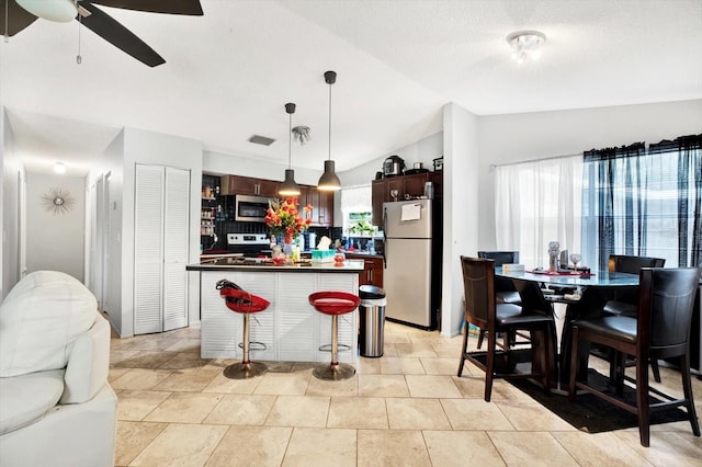 kitchen with ceiling fan, a center island, stainless steel appliances, decorative light fixtures, and vaulted ceiling