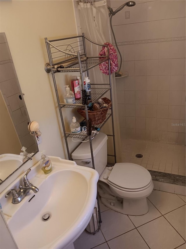 bathroom with tile patterned floors, toilet, a tile shower, and sink