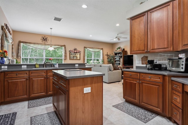 kitchen featuring ceiling fan, pendant lighting, sink, decorative backsplash, and a center island