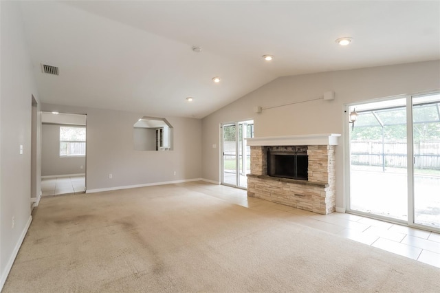 unfurnished living room featuring lofted ceiling, a wealth of natural light, tile patterned flooring, and a stone fireplace