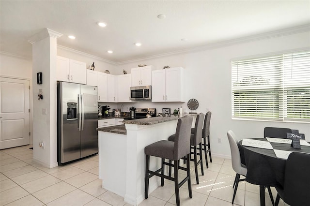 kitchen with dark stone counters, white cabinetry, kitchen peninsula, stainless steel appliances, and crown molding