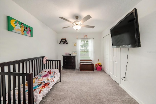 bedroom with a crib, ceiling fan, light colored carpet, and a closet