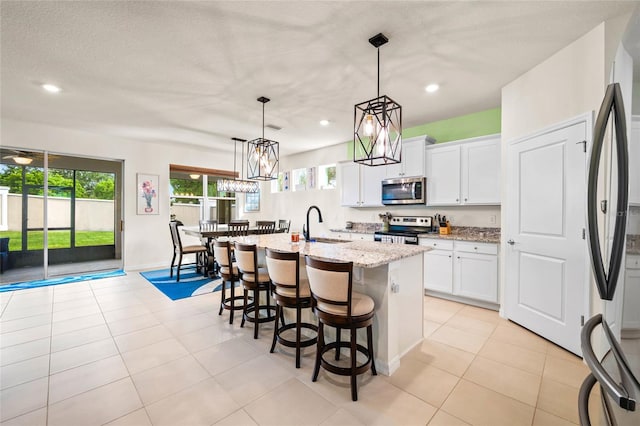 kitchen with a kitchen island with sink, white cabinetry, pendant lighting, and stainless steel appliances