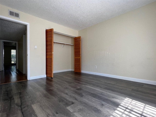 unfurnished bedroom with a textured ceiling, dark hardwood / wood-style floors, and a closet