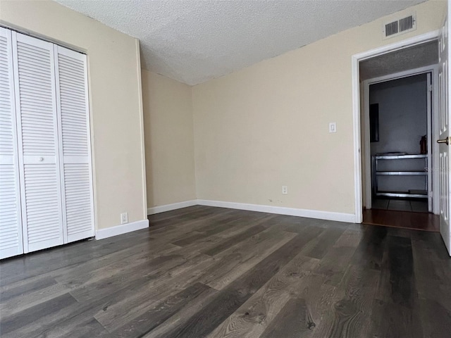 unfurnished bedroom with a textured ceiling, dark wood-type flooring, and a closet