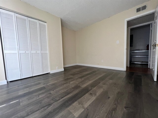 unfurnished bedroom featuring a textured ceiling, a closet, and dark wood-type flooring