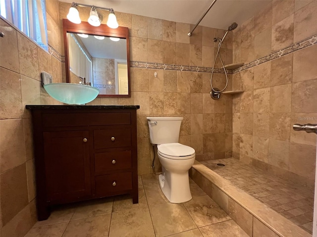 bathroom with tile walls, tile patterned floors, tiled shower, vanity, and toilet