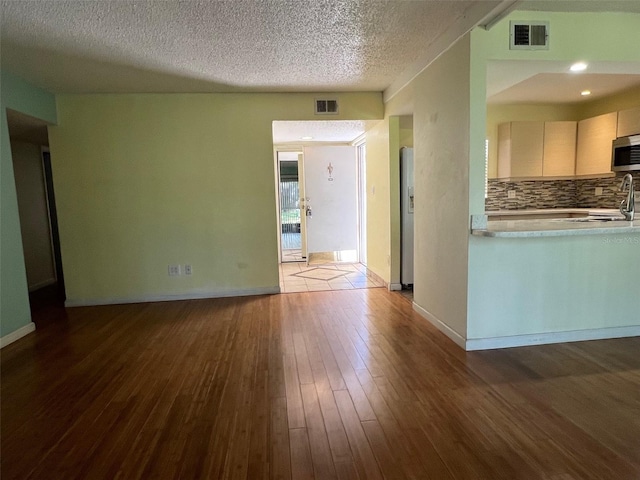 interior space featuring a textured ceiling, appliances with stainless steel finishes, backsplash, and dark hardwood / wood-style flooring