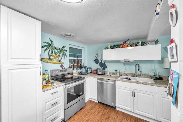 kitchen with appliances with stainless steel finishes, white cabinets, a textured ceiling, light wood-type flooring, and sink