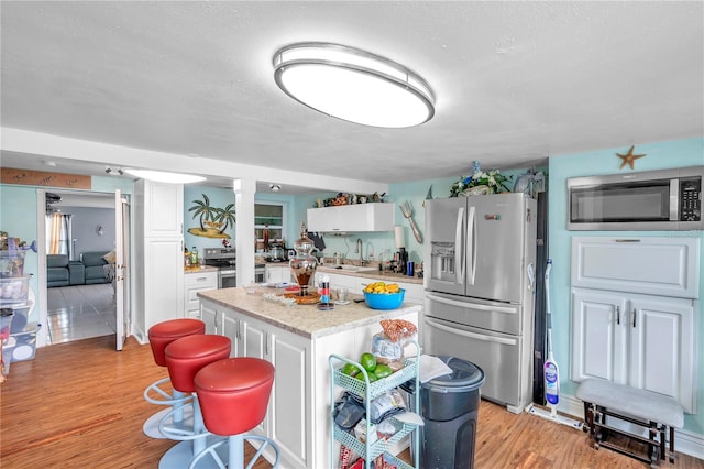 kitchen featuring appliances with stainless steel finishes, white cabinetry, a kitchen island, light wood-type flooring, and a textured ceiling